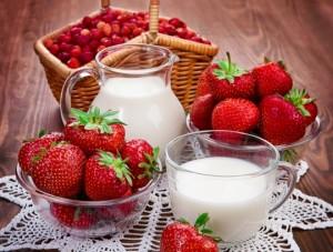 кувшин и стакан с молоком среди ягод клубники